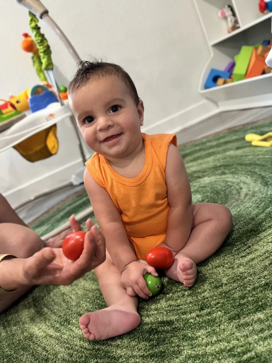 A smiling baby sitting up and playing at Firefly Family Collective
