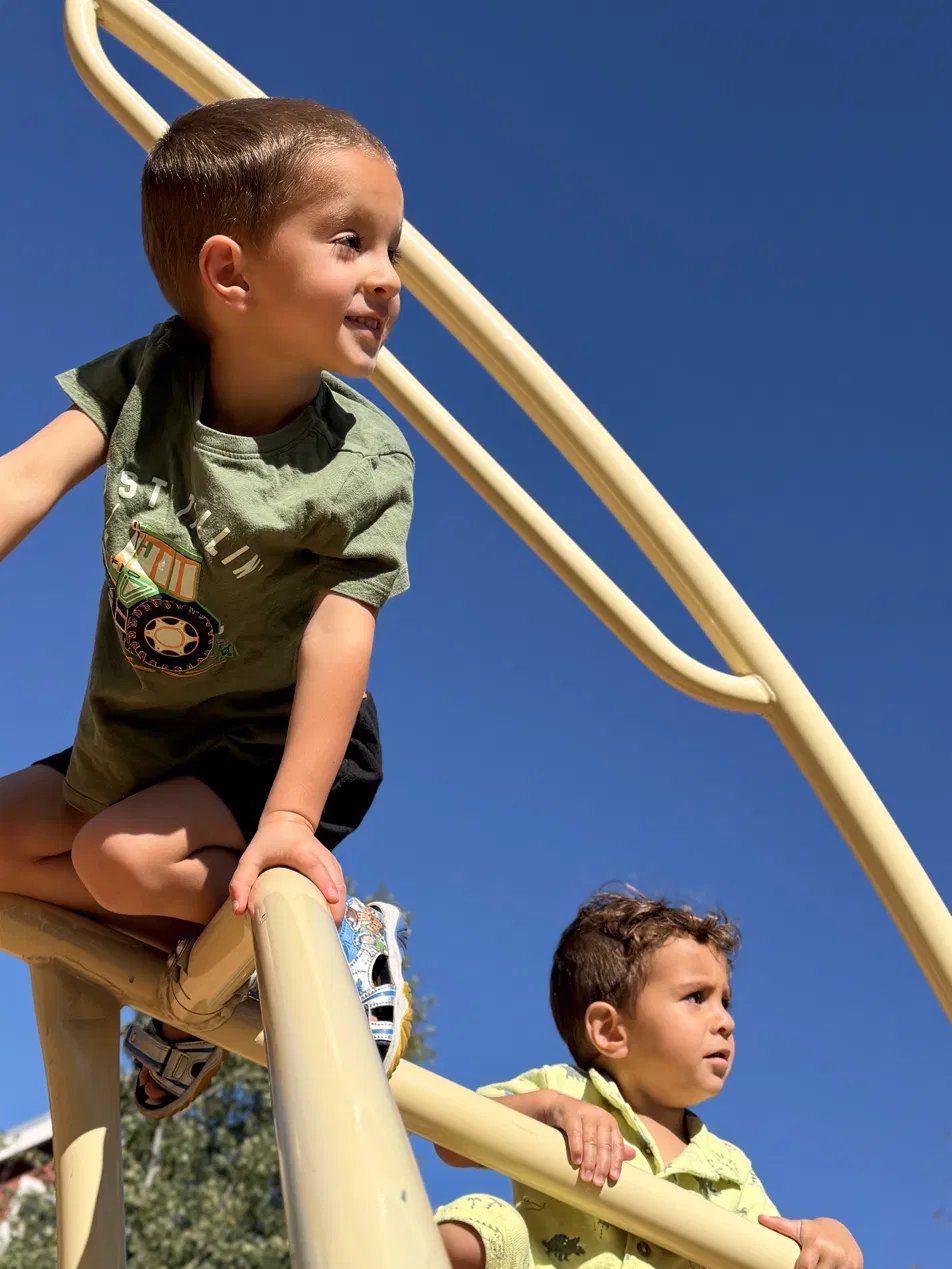 Two children climbing together under a blue sky