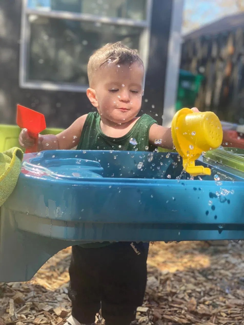 A toddler pouring water at the outdoor water table
